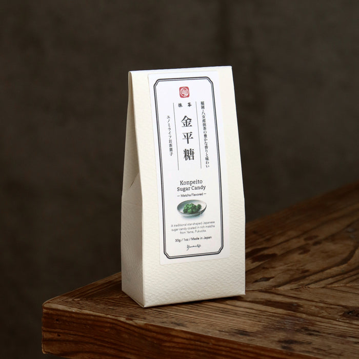 A white paper bag of Japanese Kompetto Sugar Candy standing on a rustic wooden surface against a dark brown background.